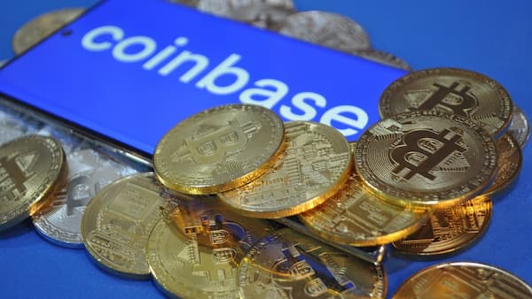 Coinbase company logo on a smart phone, surrounded by physical bitcoins.